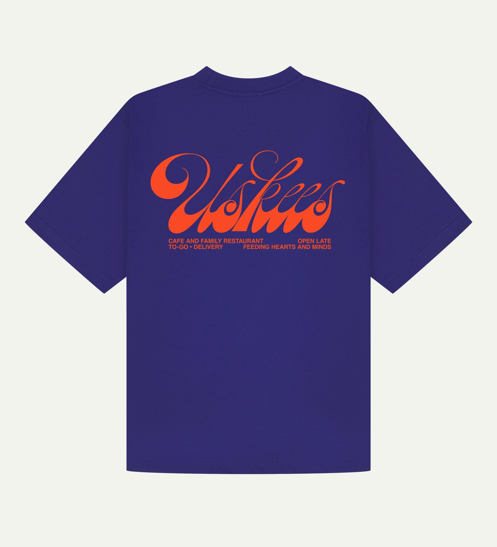 Back flat view of oversized ultra blue organic cotton Uskees short-sleeved T-shirt showing the loose silhouette. Spanning the back is the large, bright orange 'diner' logo.