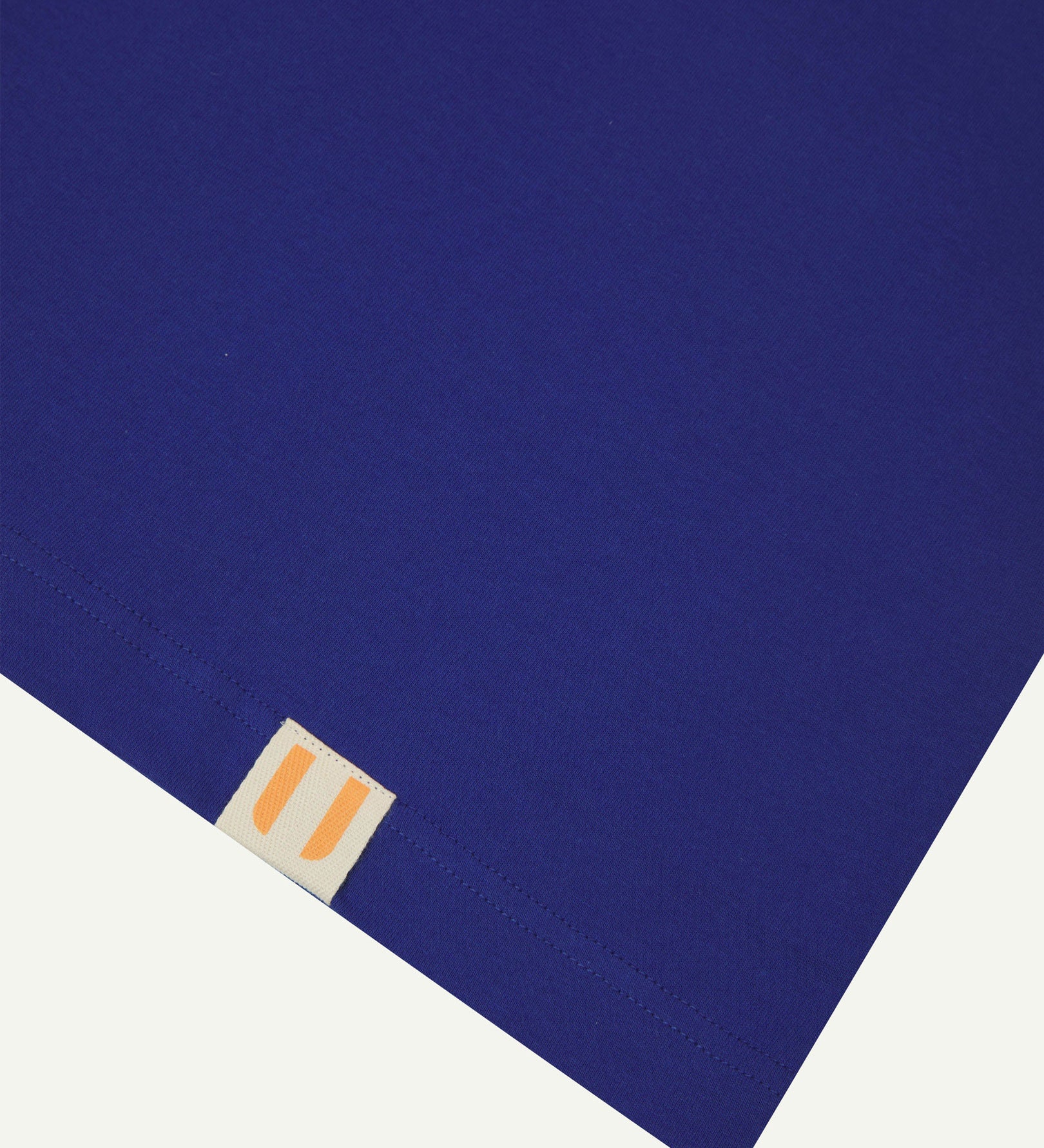 Hem close-up of ultra blue organic cotton baggy T-shirt showing square Uskees branding label.