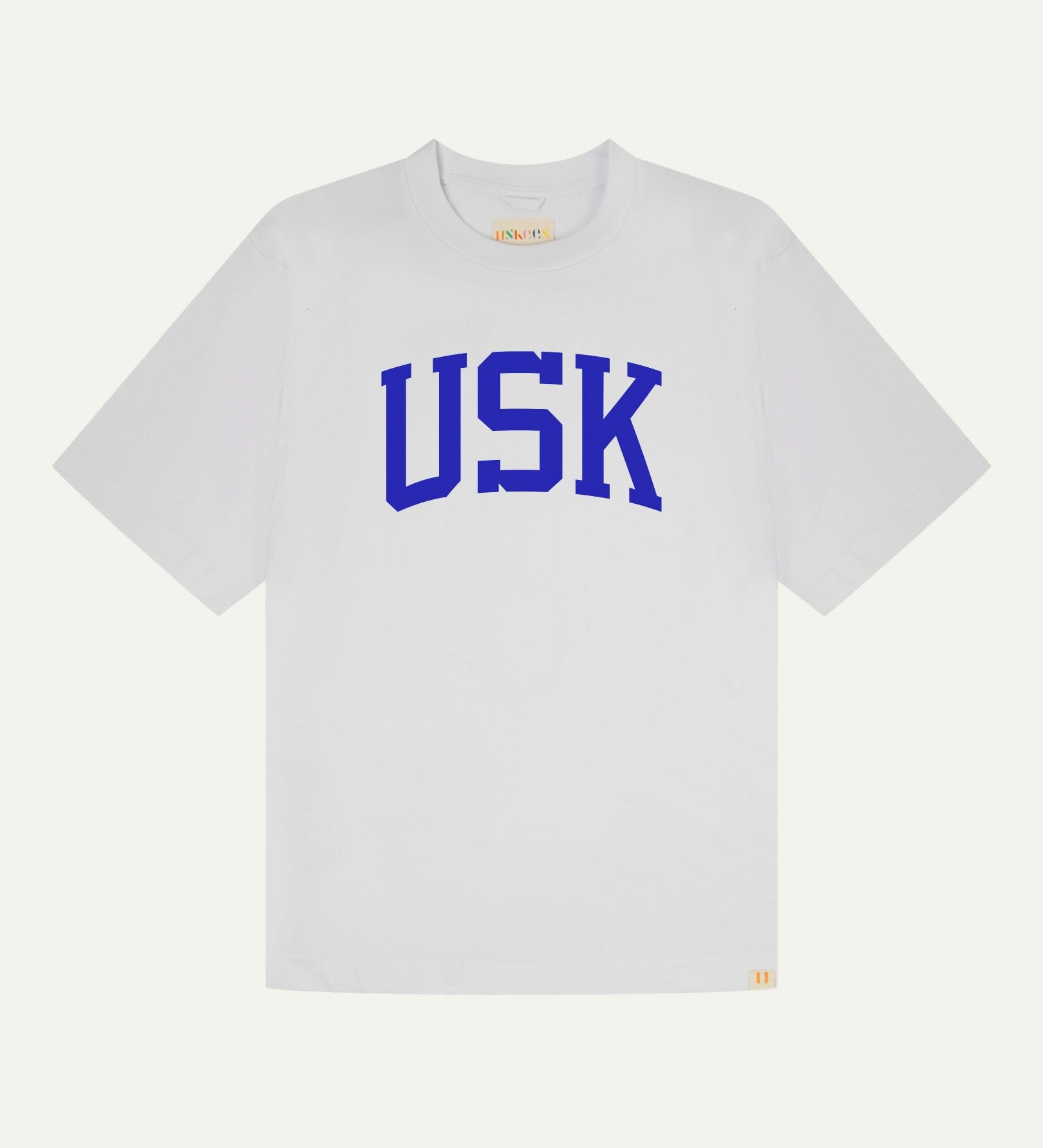 Full flat view of oversized white organic cotton signature T-shirt for men, showing the varsity inspired 'USK' logo in blue on the chest, and the Uskees branding labels on the neck and hem.