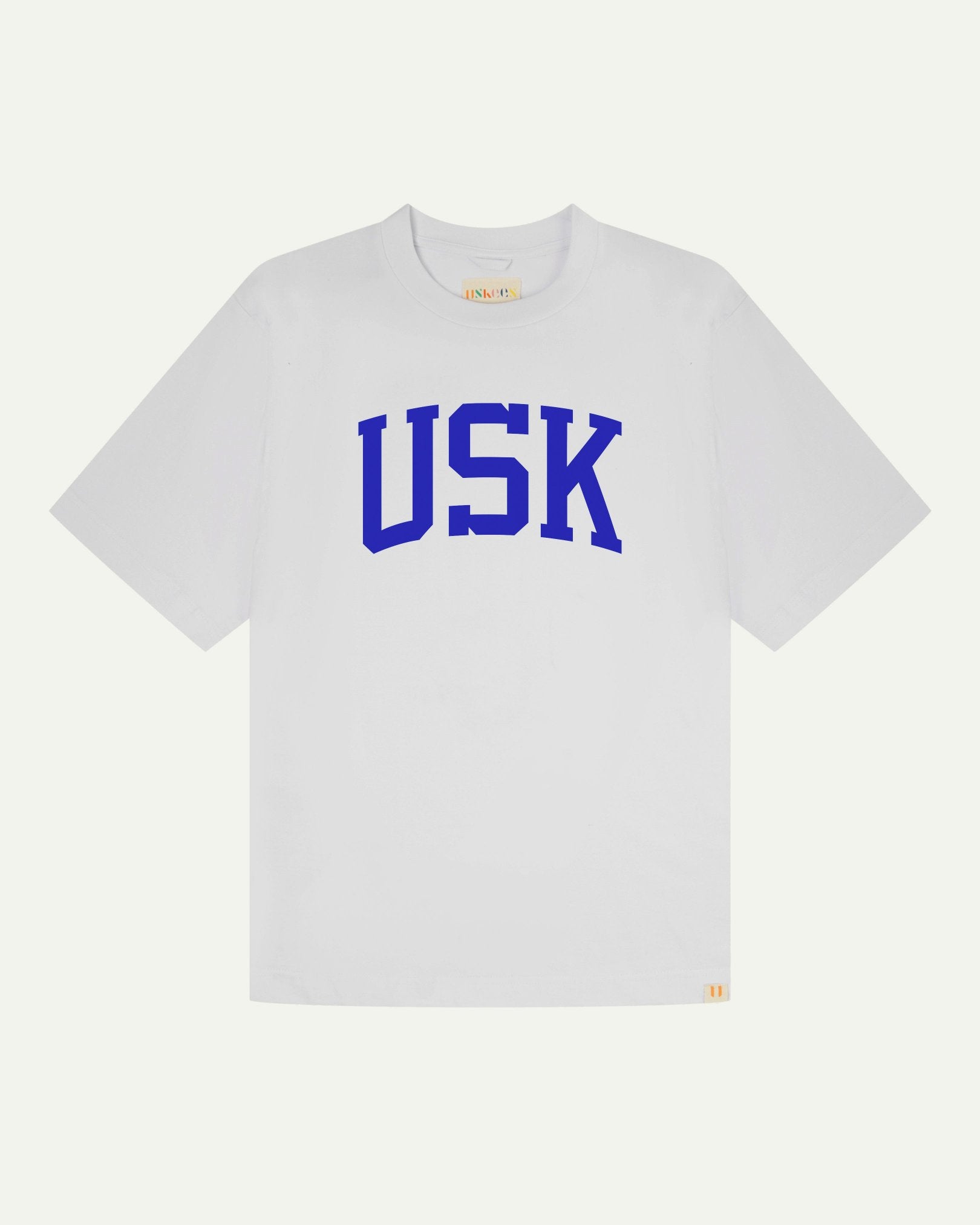 Full flat view of oversized white organic cotton signature T-shirt for men, showing the varsity inspired 'USK' logo in blue on the chest, and the Uskees branding labels on the neck and hem.