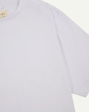 Sleeve and neckline close-up of white, organic cotton oversized T-shirt showing hanging loop and Uskees branding label.