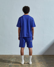 Full-length back view of model wearing striking ultra blue organic cotton #7008 oversized jersey T-shirt by Uskees paired with matching shorts.
