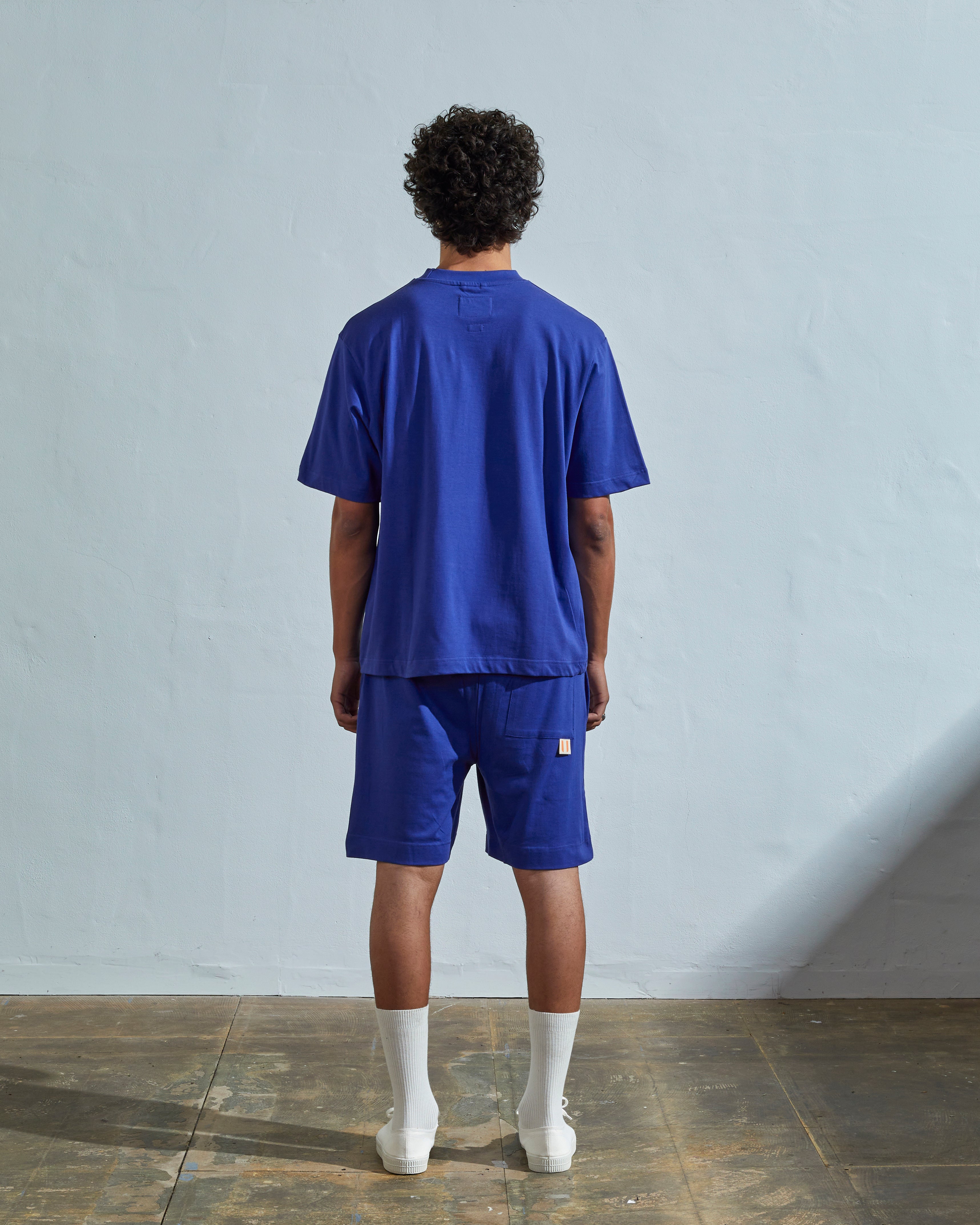 Full-length back view of model wearing striking ultra blue organic cotton #7008 oversized jersey T-shirt by Uskees paired with matching shorts.