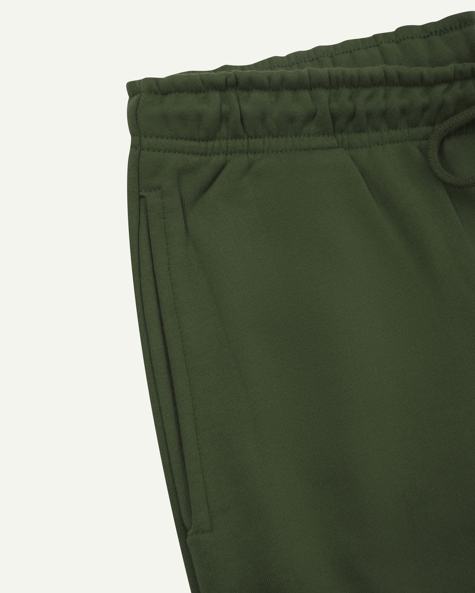 Close up view of organic cotton joggers in coriander-green showing the side pocket and drawstring waist.