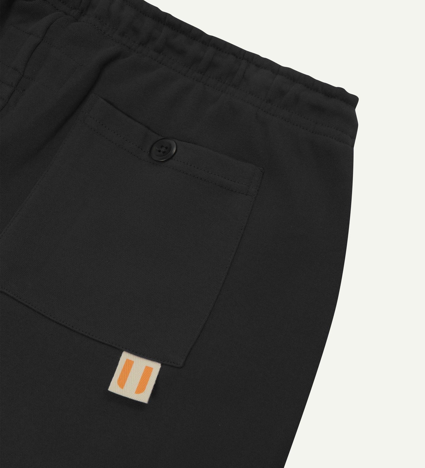 Back close view of faded black organic cotton joggers by Uskees showing the buttoned back pocket and logo label.