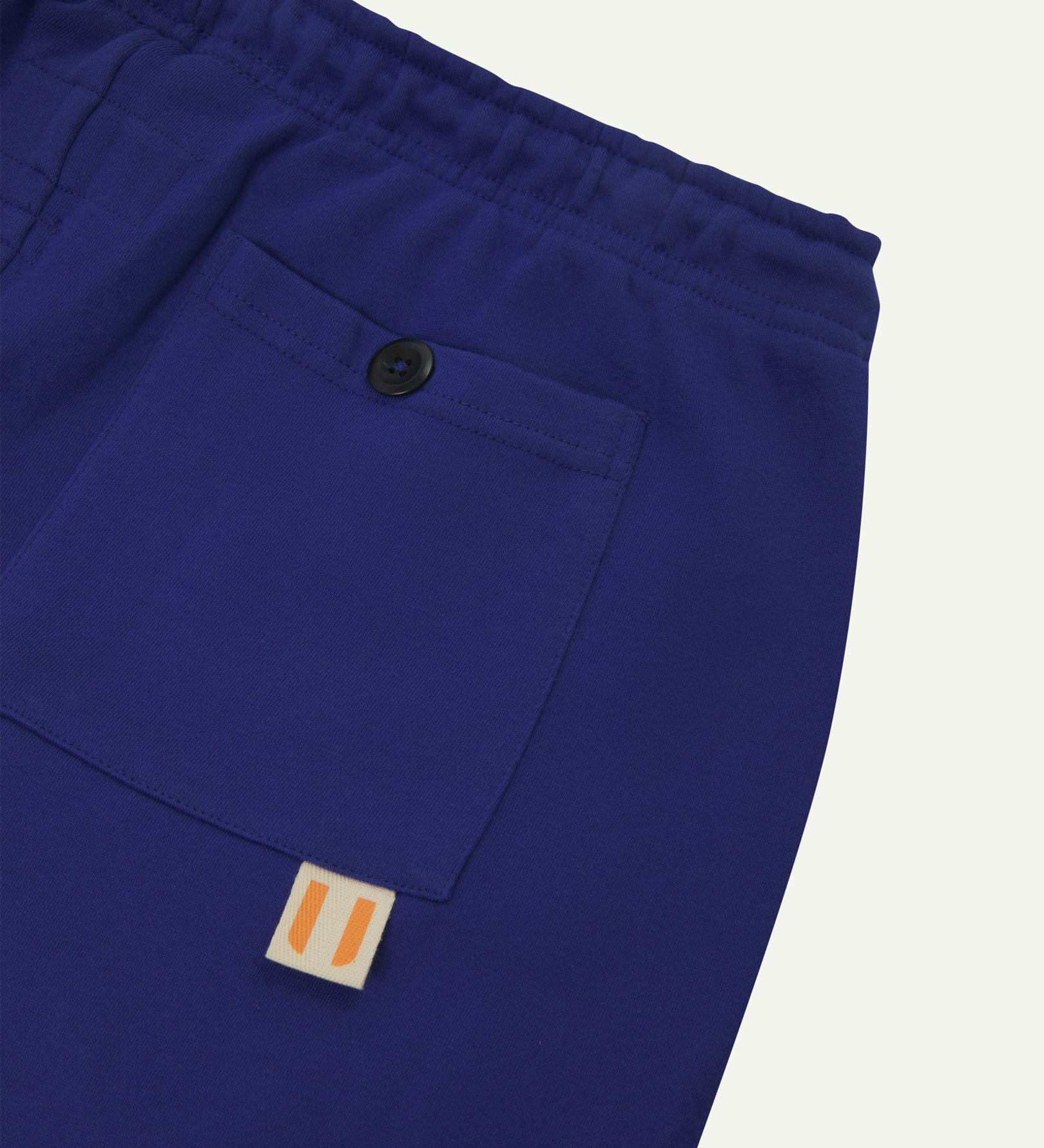 Back close view of ultra blue organic cotton joggers by Uskees showing the buttoned back pocket and logo label.