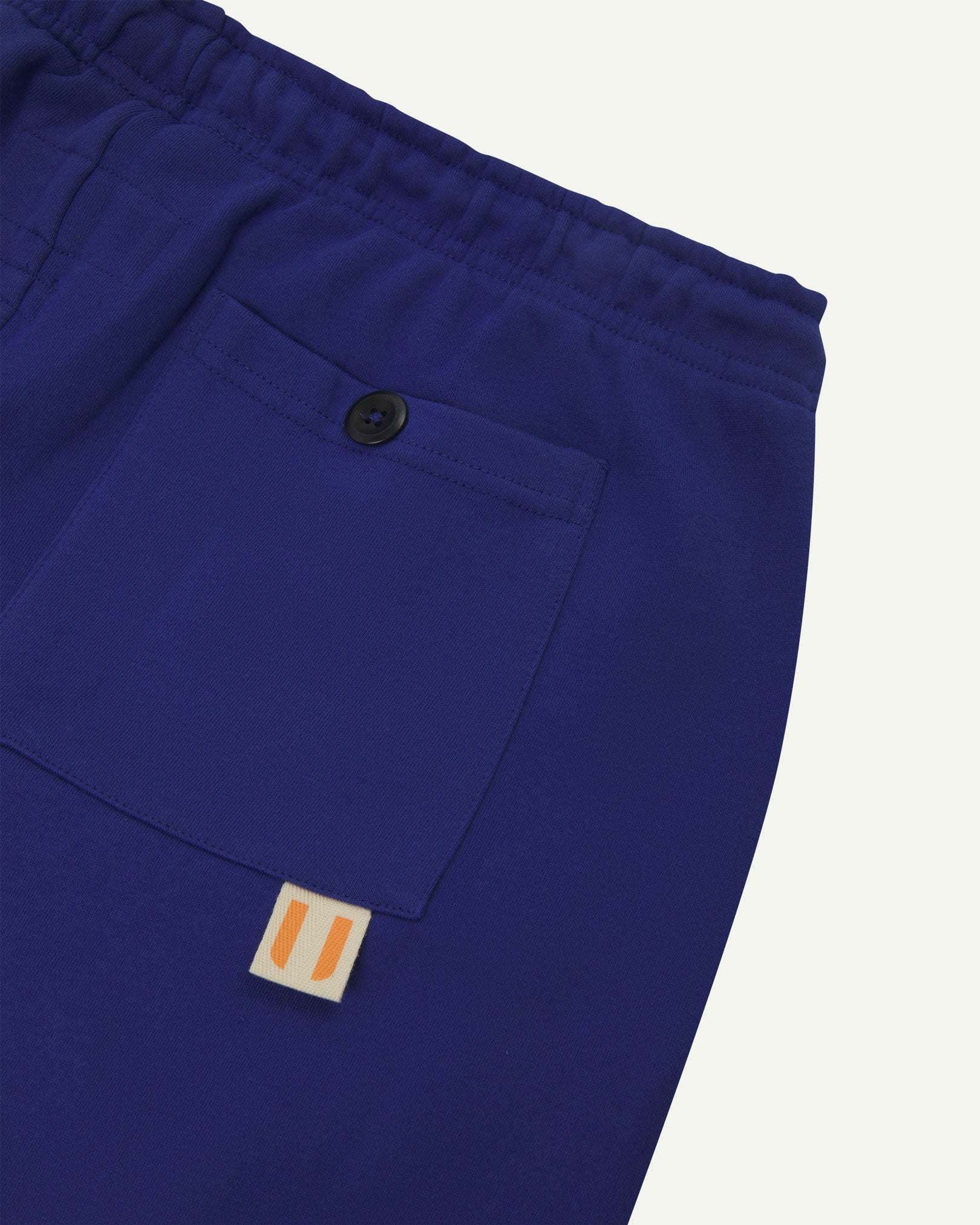 Back close view of ultra blue organic cotton joggers by Uskees showing the buttoned back pocket and logo label.