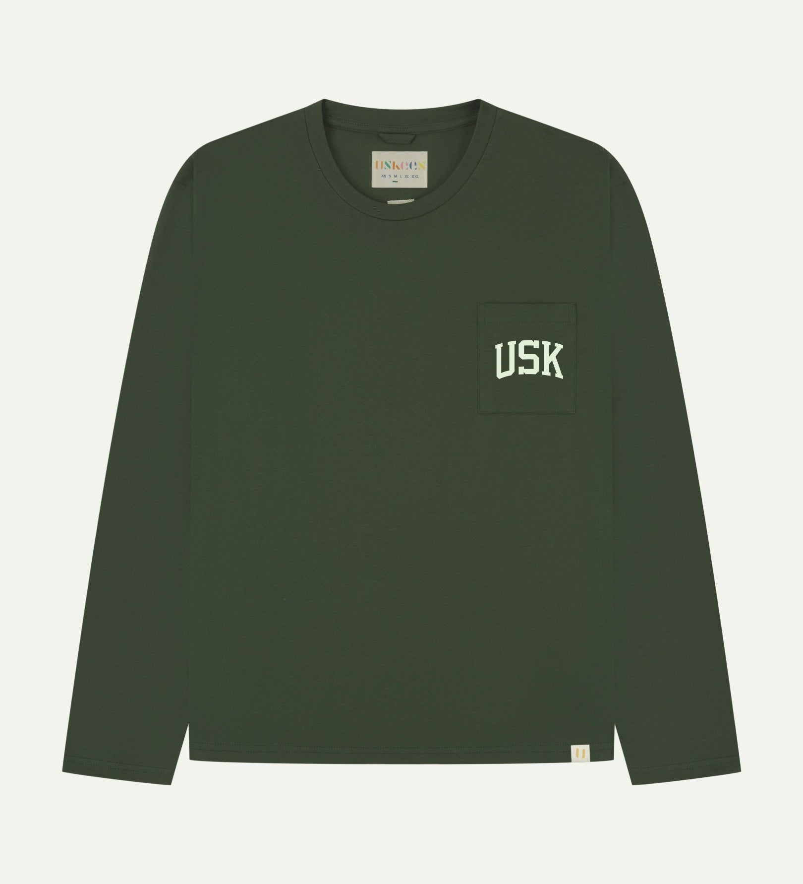 Full flat view of coriander green organic cotton signature long sleeve T-shirt for men, showing the varsity inspired 'USK' logo in white on the chest pocket, and the Uskees branding labels on the neck and hem.