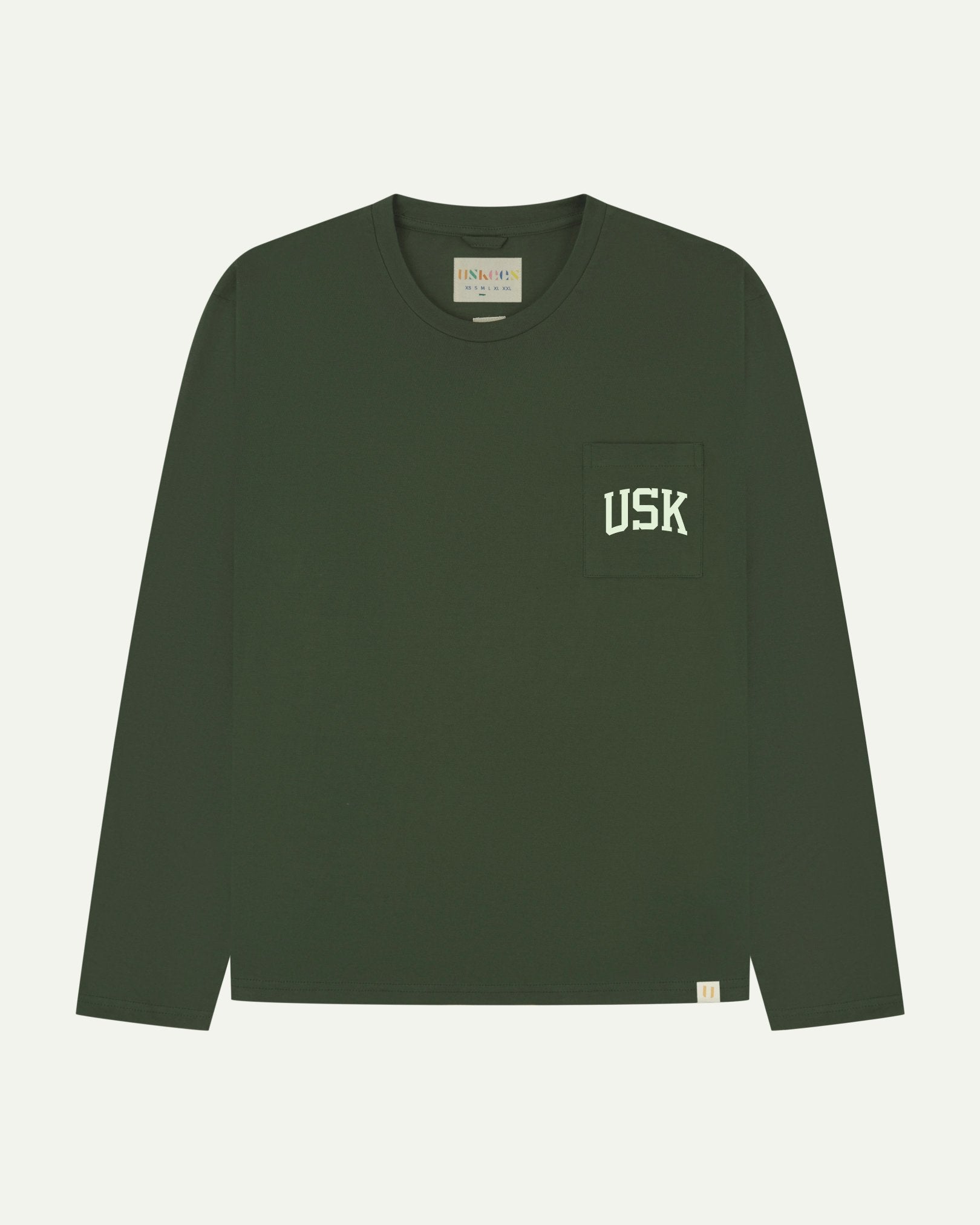 Full flat view of coriander green organic cotton signature long sleeve T-shirt for men, showing the varsity inspired 'USK' logo in white on the chest pocket, and the Uskees branding labels on the neck and hem.
