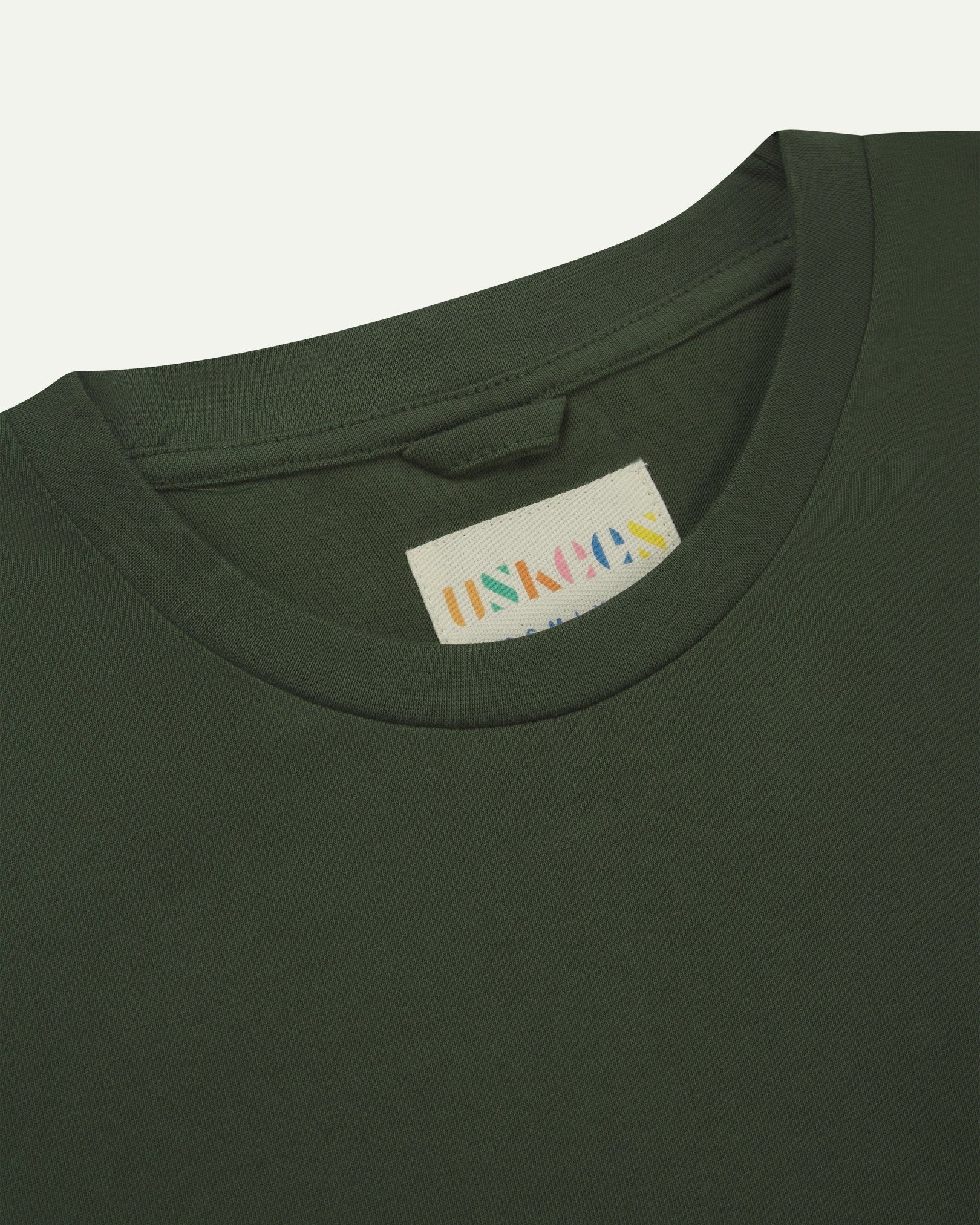 Neckline close-up of Uskees coriander-green organic cotton long-sleeved T-shirt showing hanging loop and branding label.