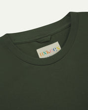 Neckline close-up of Uskees coriander-green organic cotton long-sleeved T-shirt showing hanging loop and branding label.