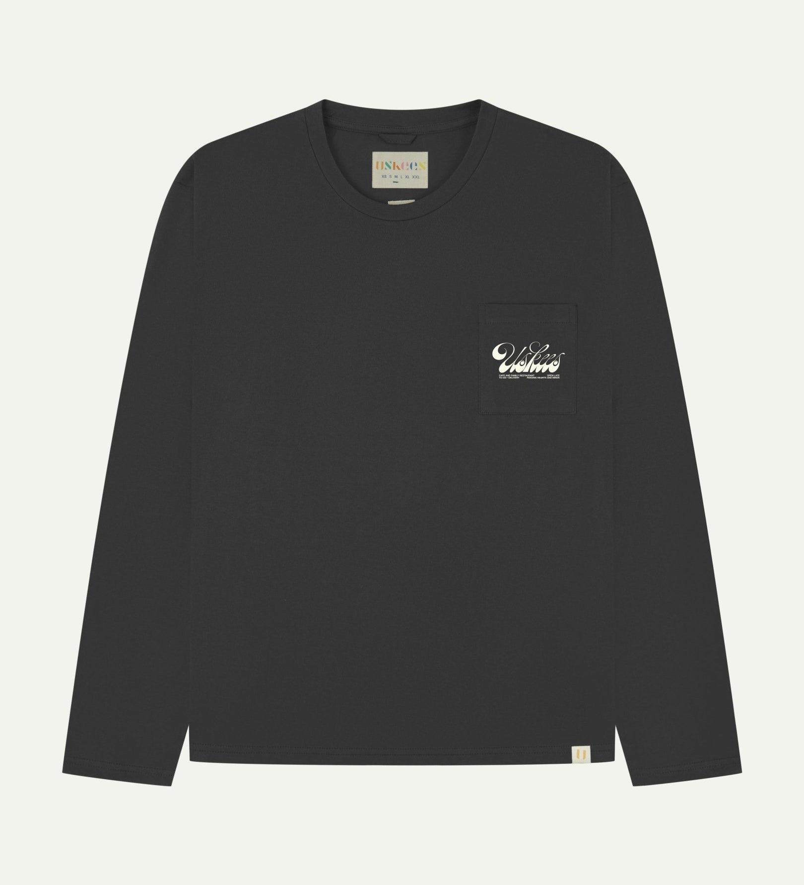 Full flat view of faded black organic cotton Uskees long-sleeve T-shirt for men, showing the small white 'diner' logo on the breast pocket and the Uskees branding labels on the neck and hem.