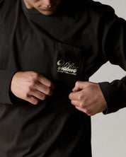 Front view wearing the uskees men's 'diner' long-sleeve tee in faded black demonstrating the loose, relaxed fit and highlighting the white 'diner' logo on the breast pocket.