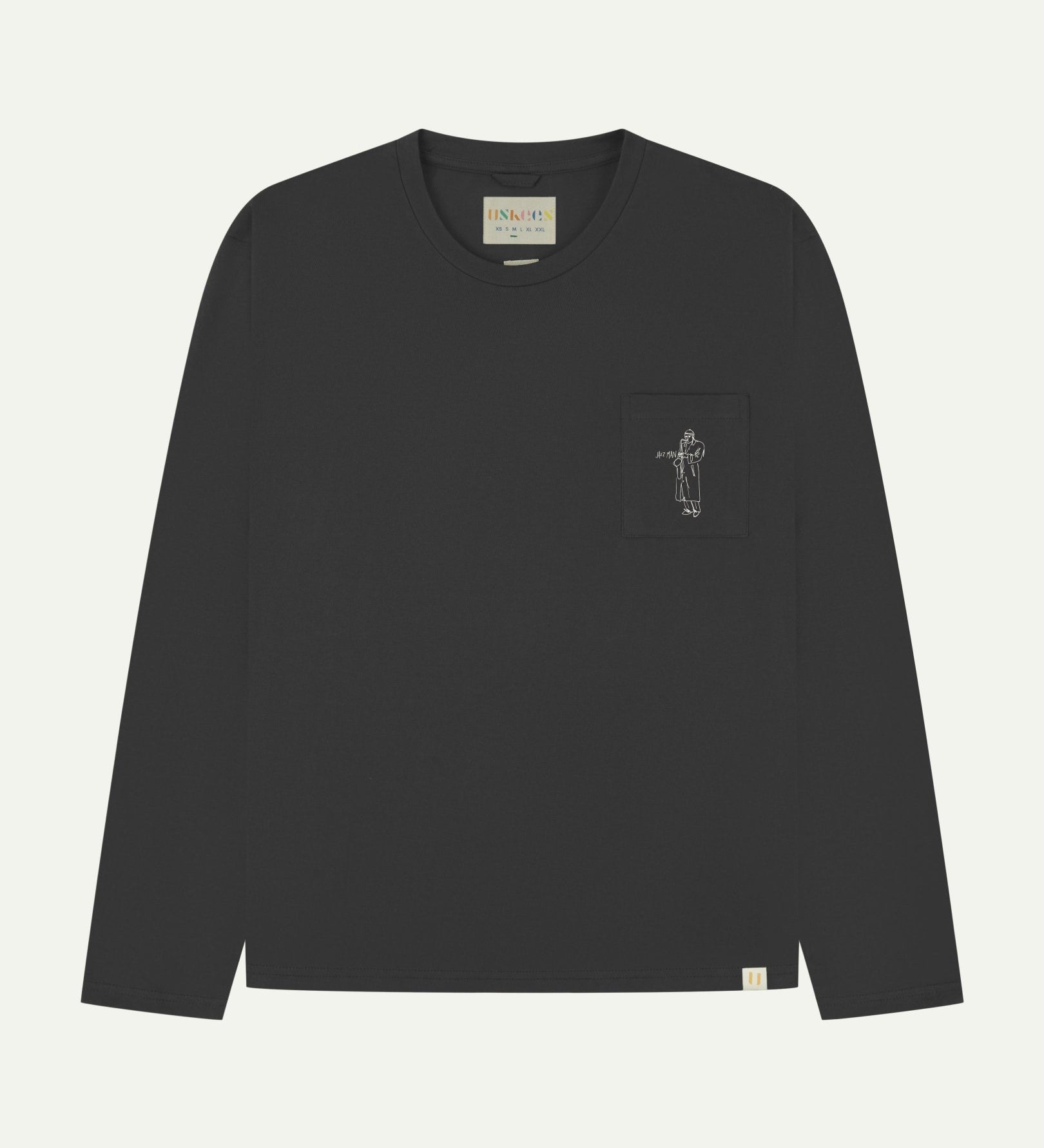 Full flat view of faded black organic cotton Uskees long-sleeve T-shirt for men, showing the small white 'Jazz Man' logo on the breast pocket and the Uskees branding labels on the neck and hem.