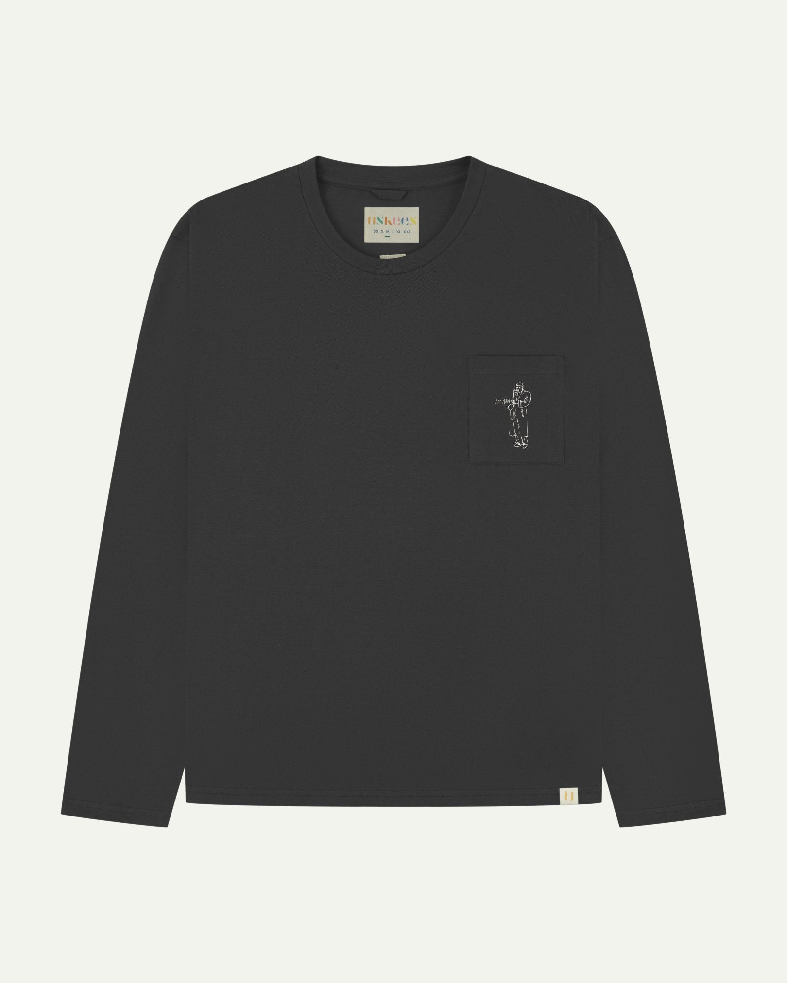 Full flat view of faded black organic cotton Uskees long-sleeve T-shirt for men, showing the small white 'Jazz Man' logo on the breast pocket and the Uskees branding labels on the neck and hem.