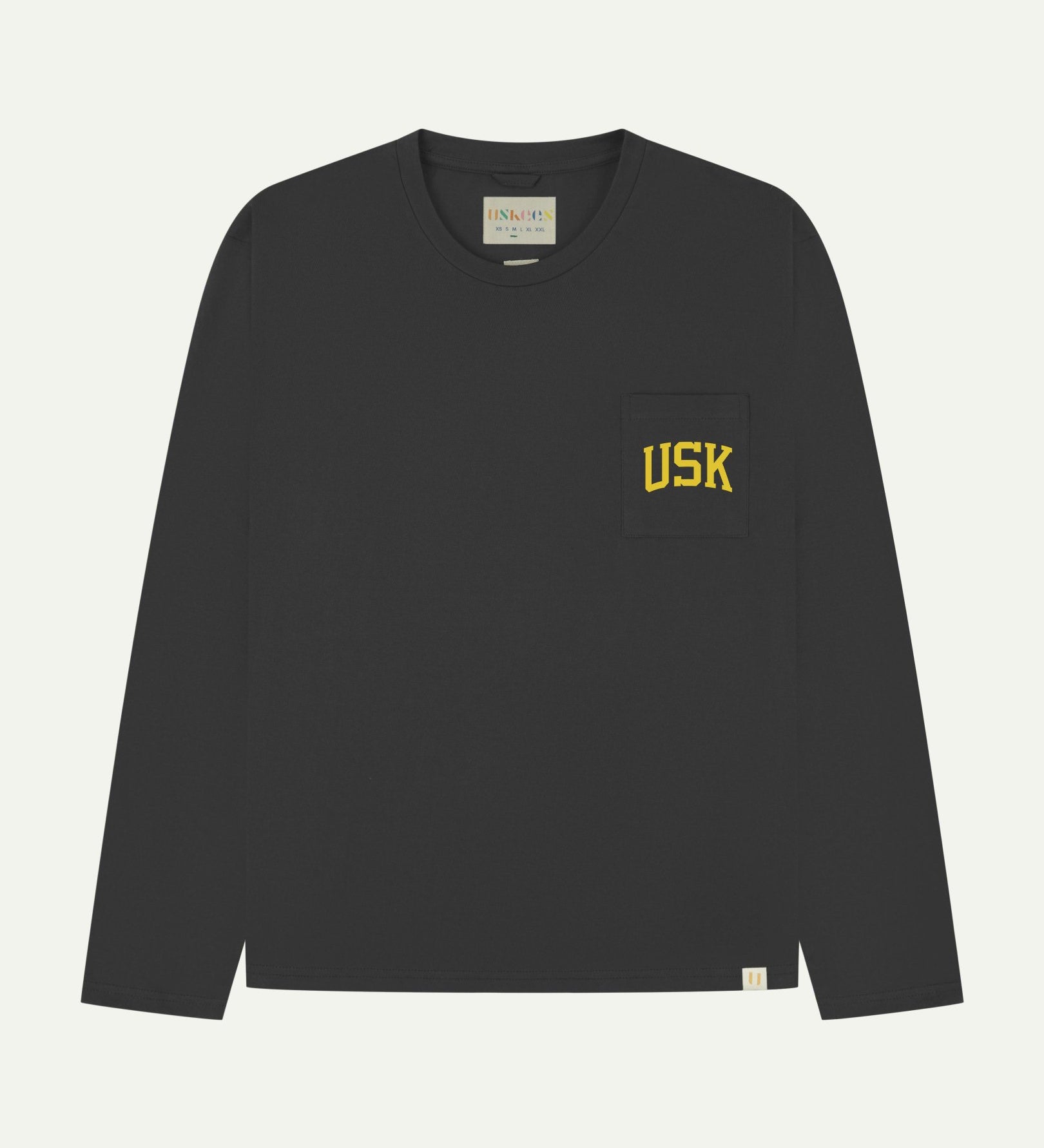 Full flat view of faded black organic cotton signature long sleeve T-shirt for men, showing the varsity inspired 'USK' logo in yellow on the chest pocket, and the Uskees branding labels on the neck and hem.