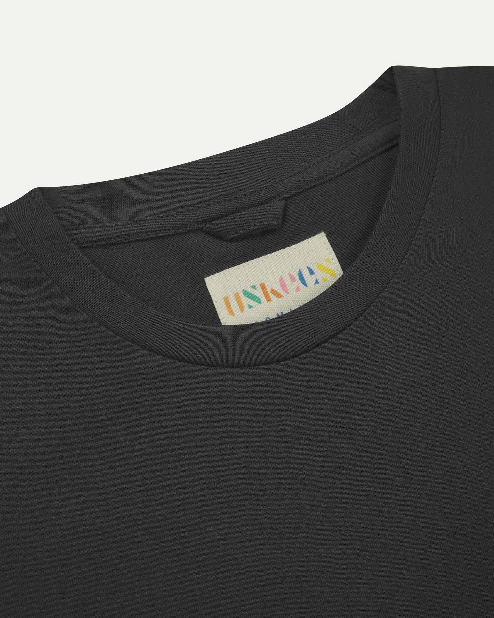 Neckline close-up of Uskees faded black organic cotton long-sleeved T-shirt showing hanging loop and branding label.