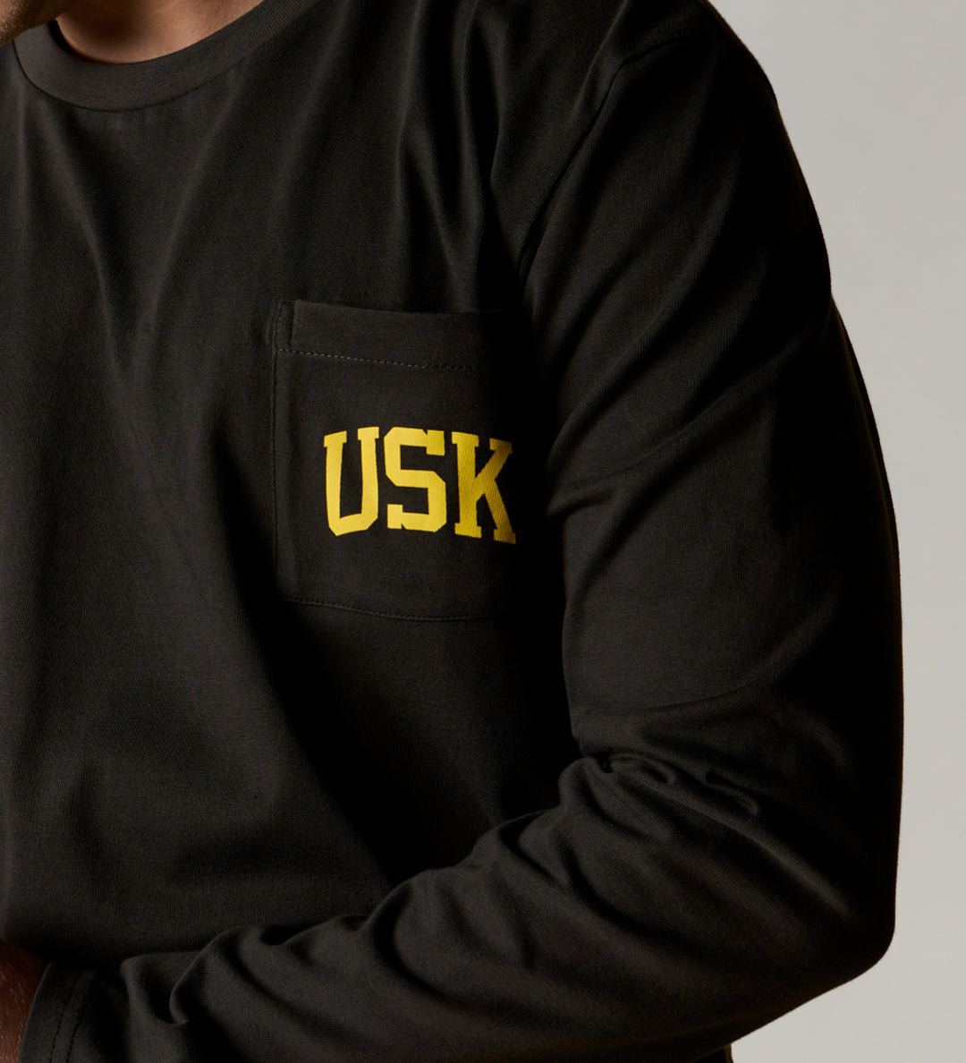 A closer front view wearing the faded black organic cotton signature long sleeve T-shirt for men, demonstrating the loose, relaxed fit with a clear view of the 'Team Uskees' logo on the chest.