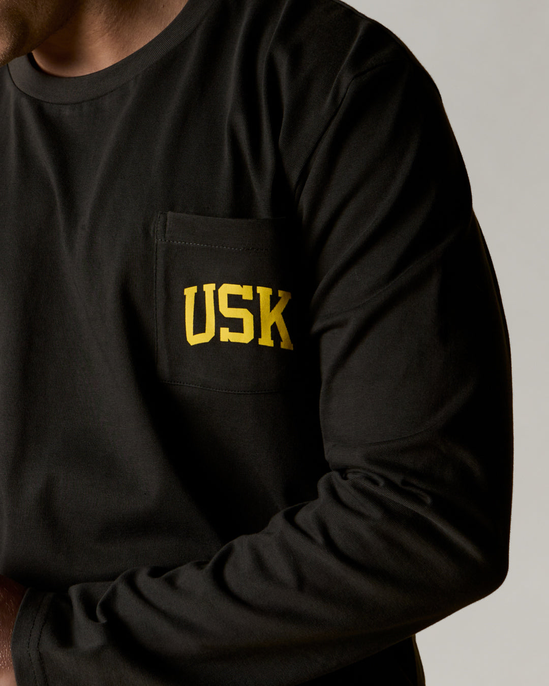 A closer front view wearing the faded black organic cotton signature long sleeve T-shirt for men, demonstrating the loose, relaxed fit with a clear view of the 'Team Uskees' logo on the chest.