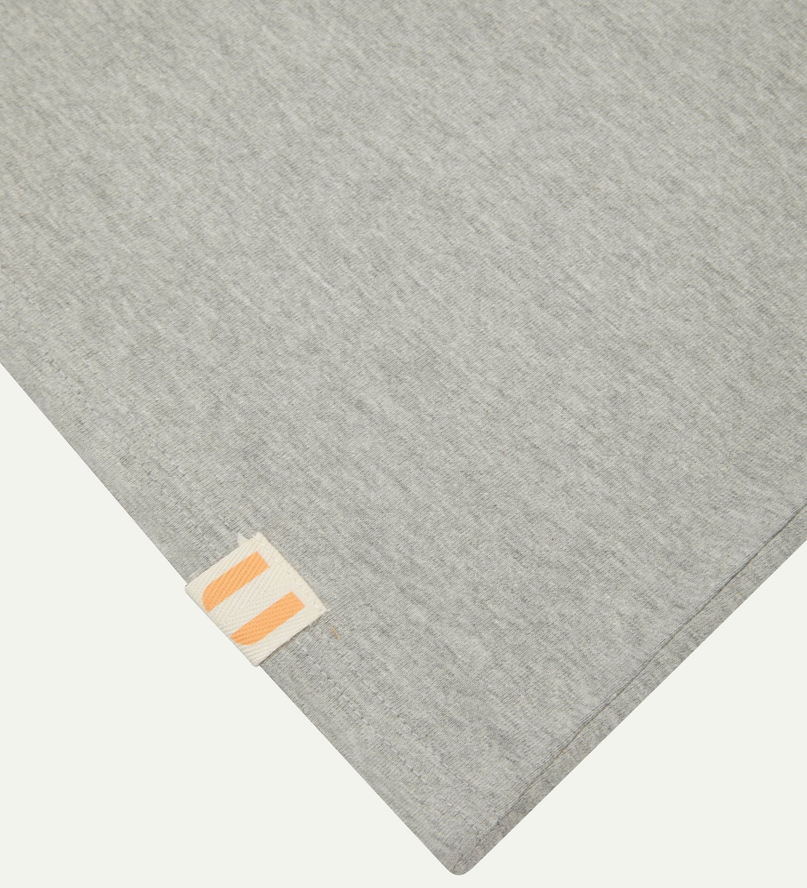 Closer look at the hem of the grey marl organic cotton long sleeve T-shirt showing texture of the medium weight organic cotton jersey and the small square Uskees branding tag.