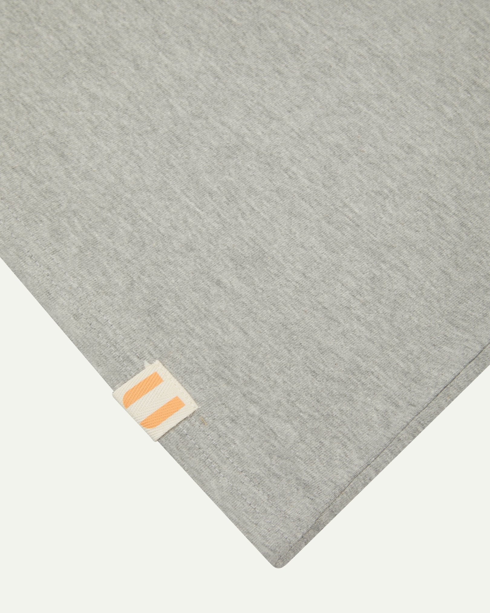 Closer look at the hem of the grey marl organic cotton long sleeve T-shirt showing texture of the medium weight organic cotton jersey and the small square Uskees branding tag.