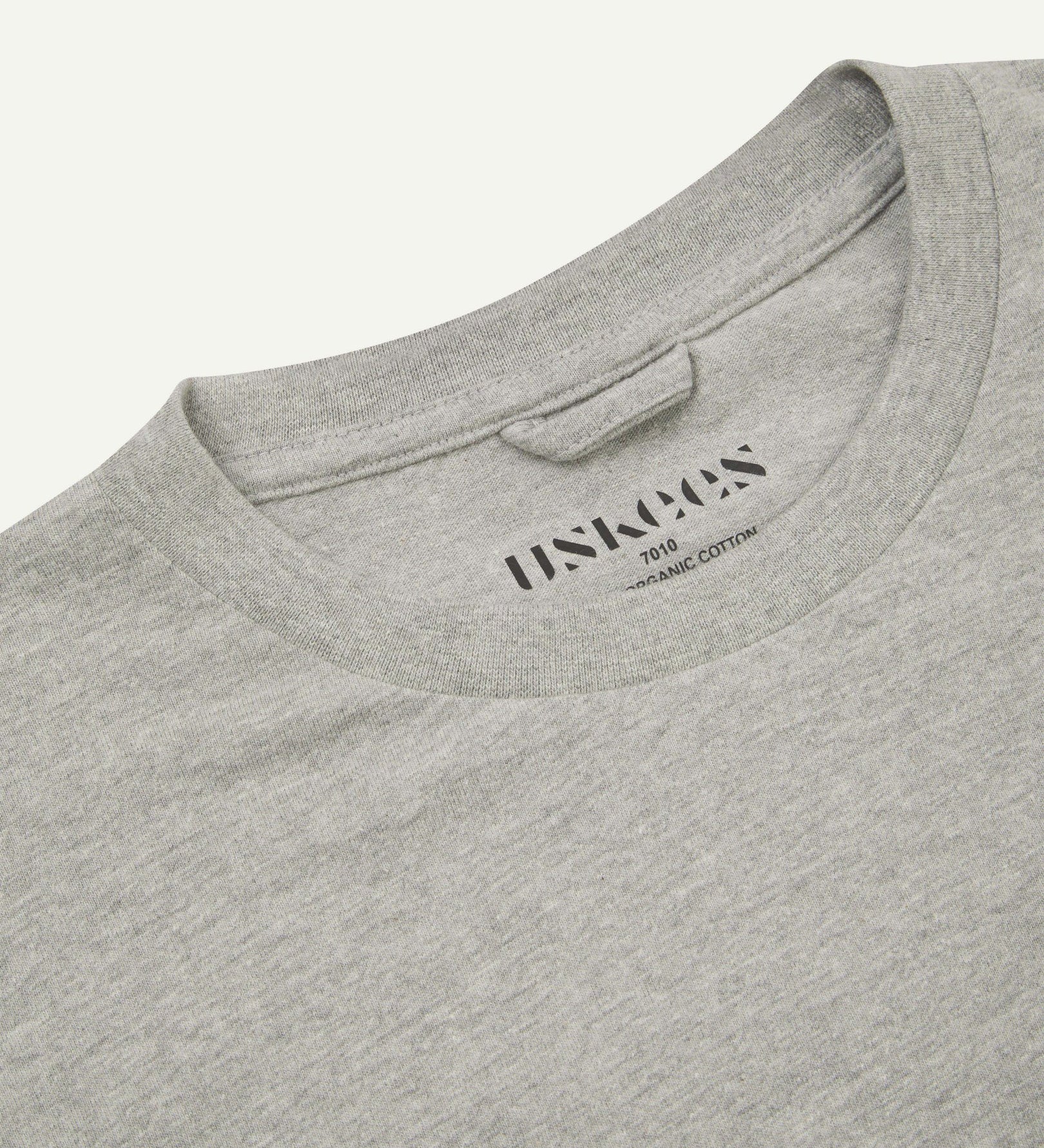 Neckline close-up of Uskees grey marl organic cotton long-sleeve T-shirt showing hanging loop and branding stamp.