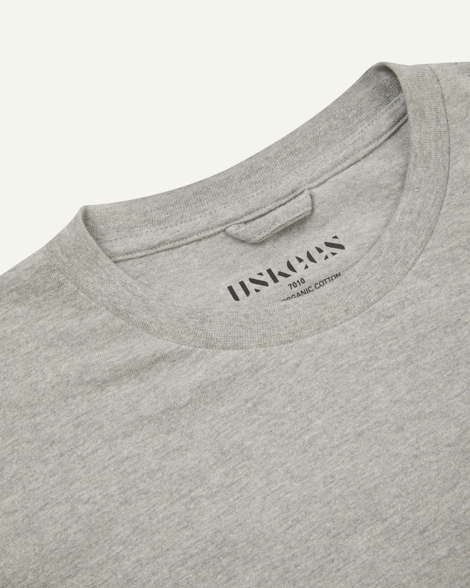 Neckline close-up of Uskees grey marl organic cotton long-sleeve T-shirt showing hanging loop and branding stamp.