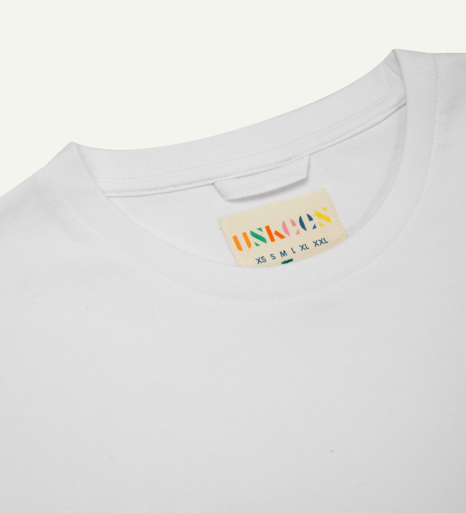 Neckline close-up of Uskees white organic cotton long-sleeved T-shirt showing hanging loop and branding label.