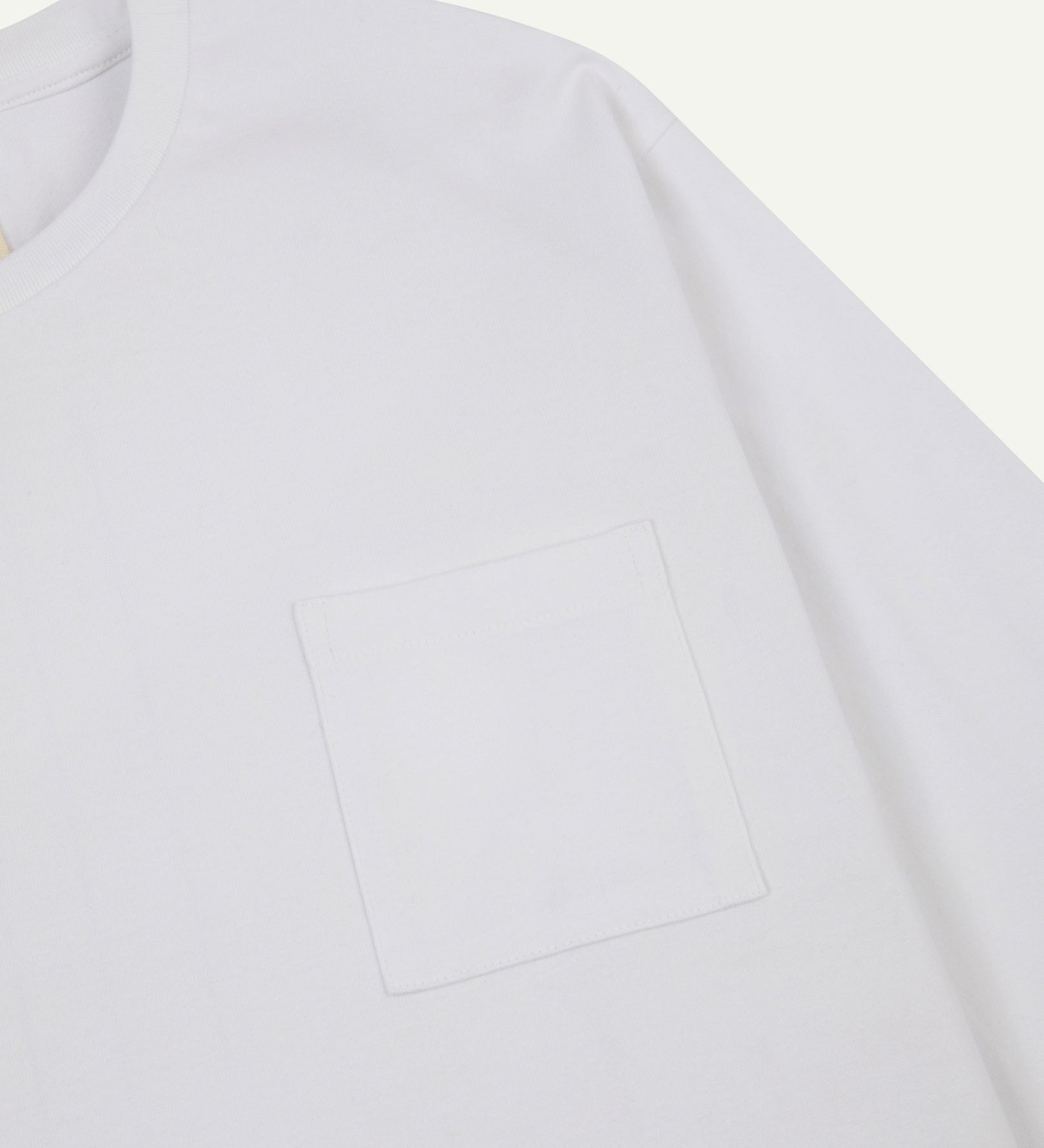Sleeve and neckline close-up of Uskees white organic cotton long-sleeved T-shirt with focus on breast pocket.