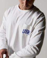 A closer front view wearing the white organic cotton signature long sleeve T-shirt for men, demonstrating the loose, relaxed fit with a clear view of the 'Team Uskees' logo on the chest.