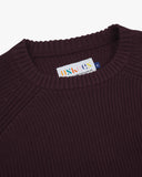 Close up view of an Uskees dark red crew knit men's jumper showing the brand label at neck.