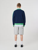Back view of a male model wearing a navy and green track jacket with light gray shorts on a white background