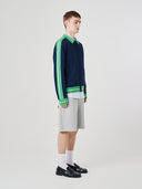Side view of a male model wearing a navy and green track jacket with light grey shorts on a white background