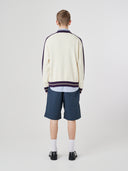 Back view of male model wearing a cream track jacket with light blue shorts on a white background