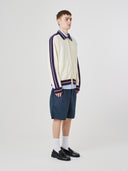 Side view of male model wearing a cream track jacket with light blue shorts on a white background