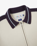 Close-up of a cream-coloured jacket with a dark purple collar, front zipper, featuring an Uskees brand label.