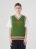 Front view of a male model wearing a bright green sleeveless sweater vest with 'USKEES' branding on the front in red.
