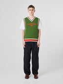 Front shot of male model wearing a green sleeveless sweater with 'USKEES' branding, paired with navy pants.