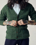 Model wearing moss-green Harris cardigan with focus on corozo buttons and soft lambswool weave.