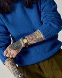 Front model shot of man wearing an Uskees ultra blue roll neck sweater with the sleeves rolled up to show tattoos, watch and bracelets.