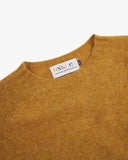 Close up view of Uskees 7021 Skye lambswool sweater in buckthorn (mustard yellow), with focus on crew neck and branding label.