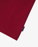 View of hemline of Uskees red cotton T-shirt with focus on cotton jersey fabric and blue 'USKEES' logo tab on the seam.