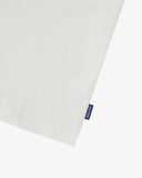 View of hemline of Uskees white cotton T-shirt with focus on cotton jersey fabric and blue 'USKEES' logo tab on the seam.