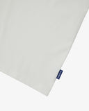 View of hemline of Uskees white cotton T-shirt with focus on cotton jersey fabric and blue 'USKEES' logo tab on the seam.
