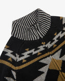 Close-up of an Uskees knit sweater featuring a black base with a geometric pattern in white and mustard yellow, and a striped ribbed mock neck collar.