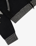 Close-up detail of an black knit cardigan with gray and black striped ribbed cuffs and hem, shown on a light gray background.
