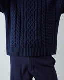 Close-up (armpit to thigh)of a navy blue cable-knit sweater worn with matching navy pants, showing the detailed knit pattern and ribbed hem against a light gray background.