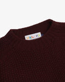Close up of an Uskees dark red Jura link jumper for men showing the neckline and brand label at neck.
