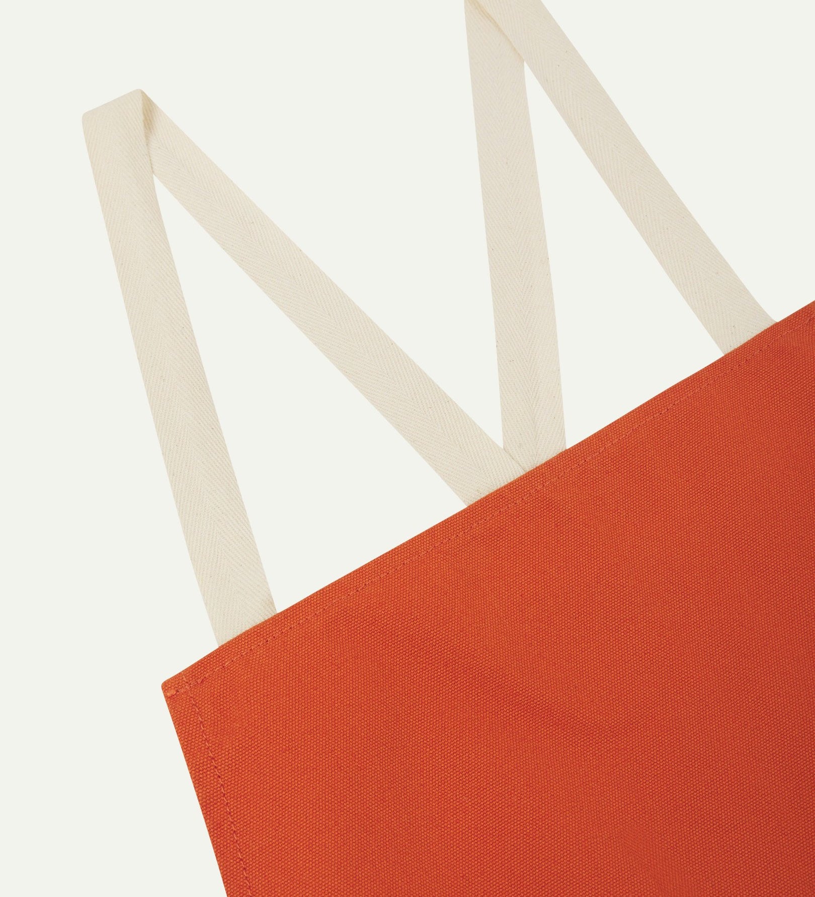 Close up angled view of Uskees unisex gold-orange canvas apron showing cream strap in an 'm' shape.