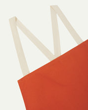 Close up angled view of Uskees unisex gold-orange canvas apron showing cream strap in an 'm' shape.